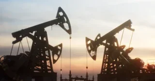 Multiple oil pump jacks working against a dramatic sunset sky. The scene highlights the industrial landscape of energy production, fossil fuels, and the petroleum industry.